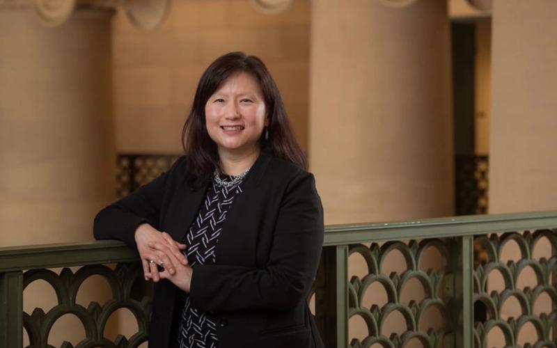Dark haired smiling woman standing with her arm propped on an ornate green metal railing.